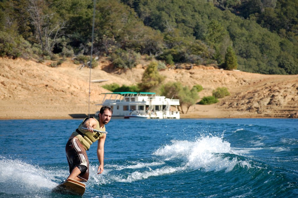 Man wakeboarding with houseboat in the background