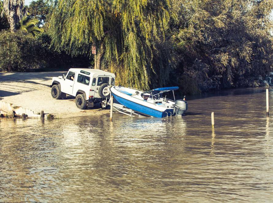 All terrain vehicle towing a trailer with a boat on top into the water.