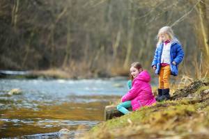 Two cute little sisters having fun by a river on warm spring day