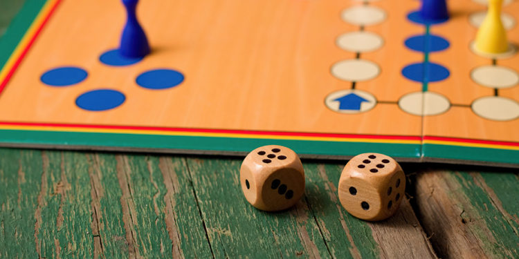 Two wooden dices in front of ludo with figurines